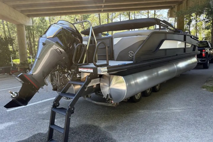 Large pontoon boat with outboard motor parked under a bridge.