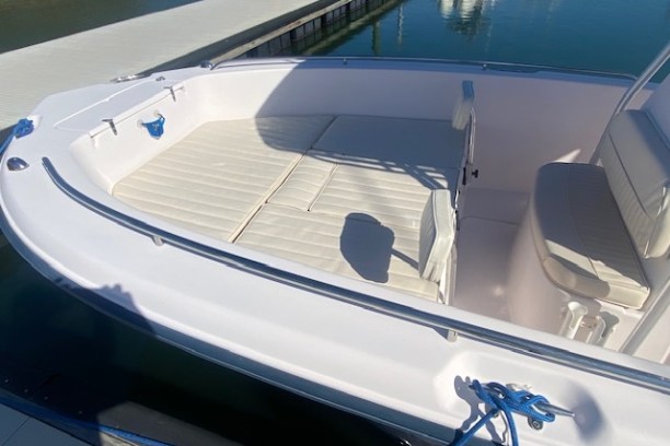 White boat interior with cushioned seating, docked by a calm waterway.