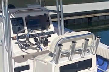 Open boat cockpit with steering wheel, rod holders, and console near a dock.