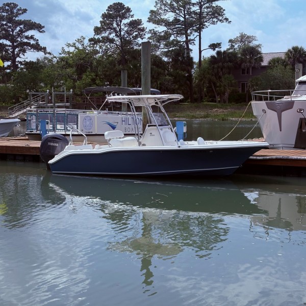 Blue and white motorboat docked on a calm waterway with trees in the background.