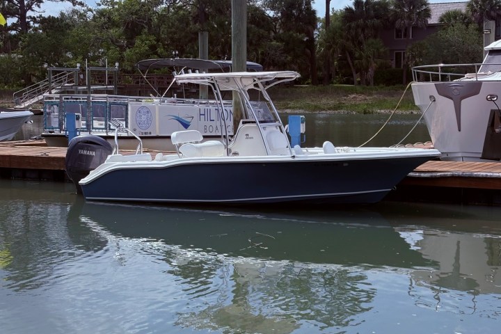 Blue and white motorboat docked on a calm waterway with trees in the background.