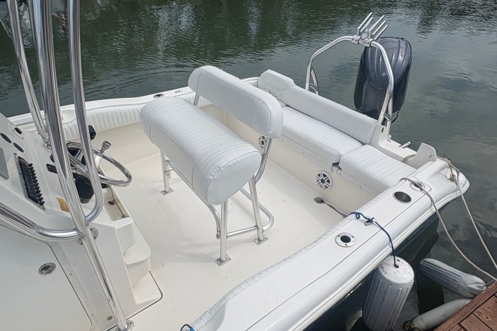White boat docked at a marina with seating and engine visible.