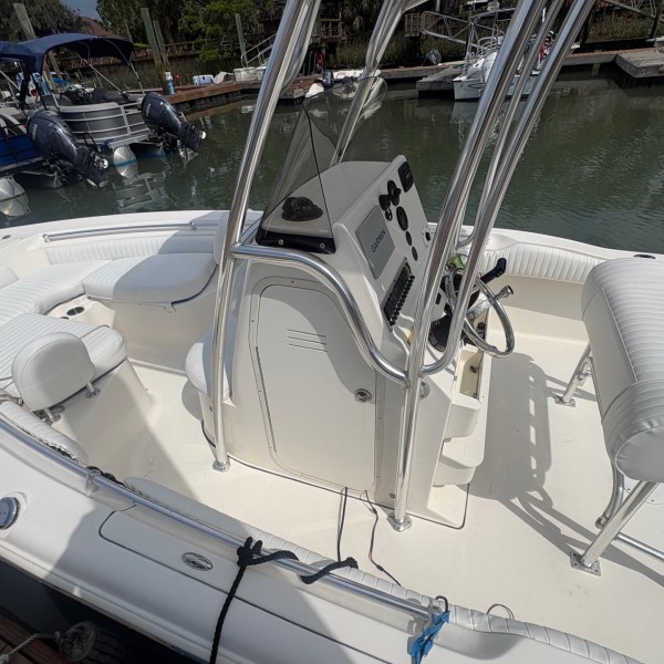 White motorboat docked by calm water with seating and control panel visible.