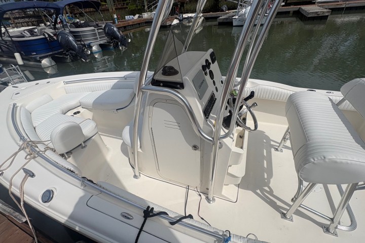 White motorboat docked by calm water with seating and control panel visible.